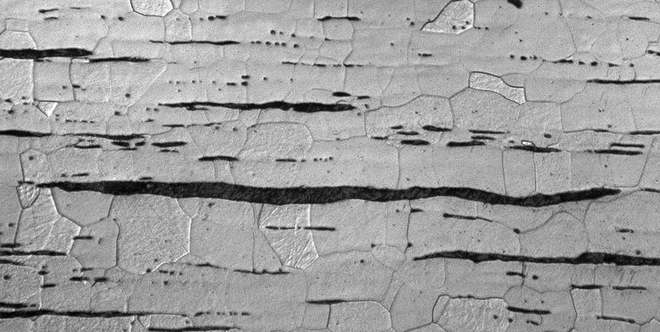 Zdjęcie stali zgrzewnej wykonane za pomocą mikroskopu optycznego. Przedstawia ciemnie, włókniste wtrącenia żużlu na tle ziaren ferrytu.
